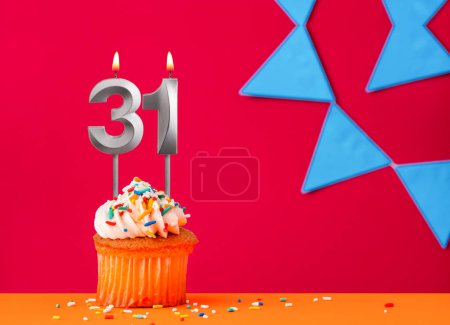 Vela número 31 con cupcake de cumpleaños sobre fondo rojo con banderines azules