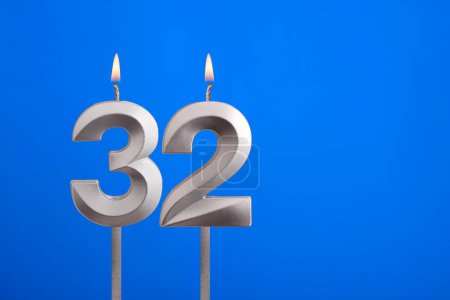 Geburtstag Nummer 32 - Kerze auf blauem Hintergrund angezündet