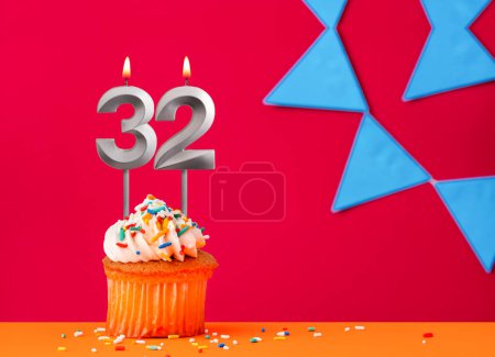 Birthday cupcake with candle number 32 on a red background with blue pennants