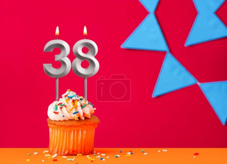 Geburtstagskuchen mit Kerze Nummer 38 auf rotem Hintergrund mit blauen Wimpeln