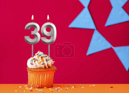 Foto de Vela número 39 con cupcake de cumpleaños sobre fondo rojo con banderines azules - Imagen libre de derechos