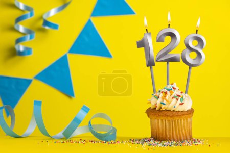 Téléchargez les photos : Bougie d'anniversaire numéro 128 avec cupcake - fond jaune avec des fanions bleus - en image libre de droit