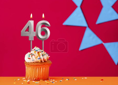 Magdalena de cumpleaños con vela número 46 sobre fondo rojo con banderines azules