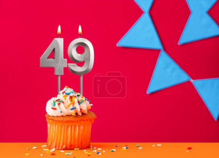 Number 49 candle with birthday cupcake on a red background with blue pennants
