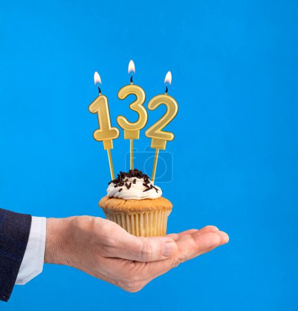 Photo for Hand delivering birthday cupcake - Candle number 132 on blue background - Royalty Free Image