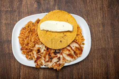 Desayuno colombiano servido en la mesa: pollo asado, arepa de maíz, queso, huevo frito y frijoles recalentados con arroz