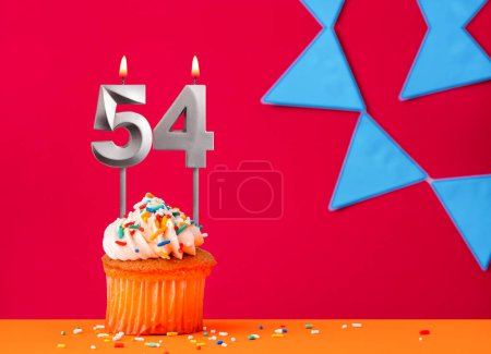 Magdalena de cumpleaños con vela número 54 sobre fondo rojo con banderines azules