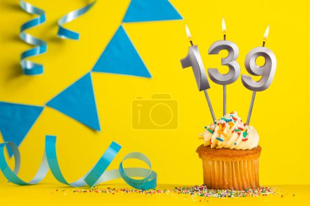 Lighted birthday candle number 139 - Yellow background with blue pennants