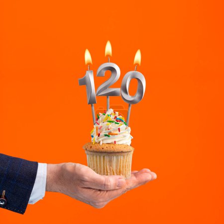 The hand that delivers cupcake with the number 120 candle - Birthday on orange background