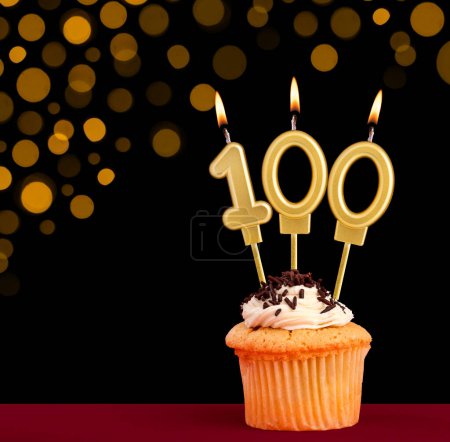 Vela de cumpleaños con cupcake - Número 100 sobre fondo negro con luces desenfocadas