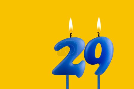 Blue birthday candle on yellow background - Number 29