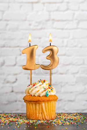 Goldene Geburtstagskerze Nummer 13 mit Cupcake - weißer Blockwandhintergrund