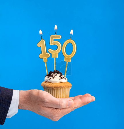 Hand liefert Geburtstagskuchen - Kerze Nummer 150 auf blauem Hintergrund