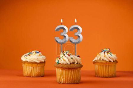 Téléchargez les photos : Bougie numéro 33 - Célébration avec cupcake d'anniversaire sur fond orange - en image libre de droit