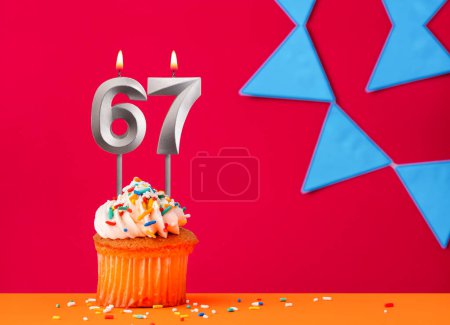 Nummer 67 Kerze mit Geburtstagskuchen auf rotem Hintergrund mit blauem Wimpel