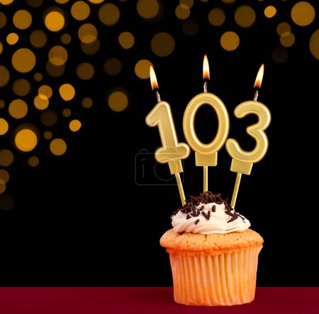 Number 103 birthday candle - Cupcake on black background with out of focus lights