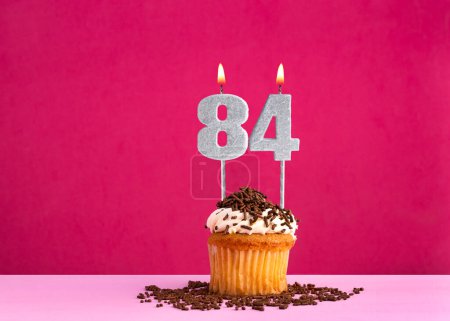 Celebración de cumpleaños con número de vela 84 - Pastel de chocolate sobre fondo rosa