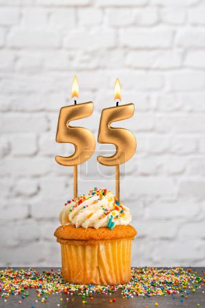 Goldene Geburtstagskerze Nummer 55 mit Cupcake - weißer Blockwandhintergrund