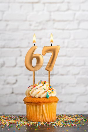 Golden birthday candle number 67 with cupcake - White block wall background