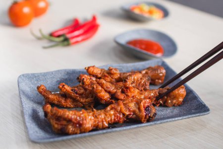 Photo for Spicy chicken feet or ceker ayam pedas with chili, tomato and sauce served with a plate on wooden white table - Royalty Free Image