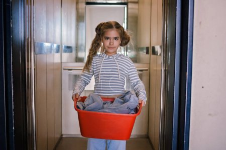 Photo for Teenage girl with a laundry basket going to common laundry. Concept of ecology, sustainability, care for environment, as well as saving money and natural resources - Royalty Free Image
