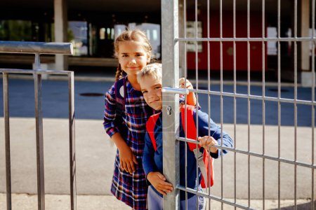 Foto de Hermanos felices con mochilas, niños de primaria, mirando desde la puerta cerca de la escuela en el primer día, estudio y educación, reunión después de las vacaciones, estilo de vida. Regreso a la escuela - Imagen libre de derechos