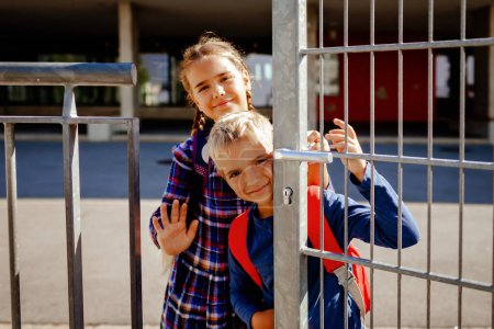 Foto de Retrato de hermanos felices con mochilas, niños de primaria, mirando desde la puerta cerca de la escuela en el primer día, estudio y educación, reunión después de las vacaciones, estilo de vida. - Imagen libre de derechos