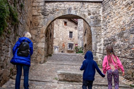 Foto de Una familia explora el encanto histórico de Perouges, Francia, pasando por un antiguo arco de piedra que conduce a calles atemporales. - Imagen libre de derechos