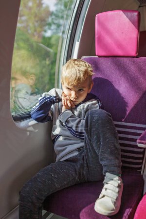 A young boy sits tensely in a train seat, gazing out the window with a hint of trepidation, reflecting the importance of ensuring child safety during travel.