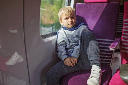 Pensive boy on train journey, sunlight accentuating his contemplative mood. A moment away from gadgets, immersed in thought.