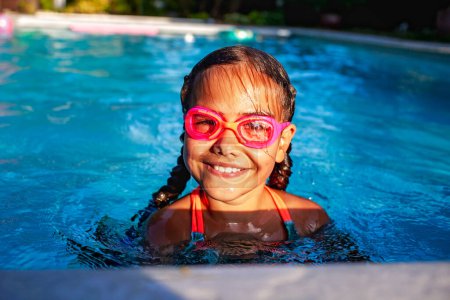 Foto de Jovencita alegre con el pelo trenzado con gafas de color rosa disfruta de un día soleado nadando en una piscina azul claro, encarnando la alegría del verano - Imagen libre de derechos