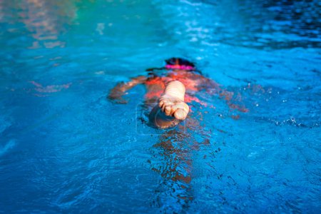 Foto de Un niño nada en una piscina azul claro, capturado desde un ángulo inusual centrándose en el pie. - Imagen libre de derechos