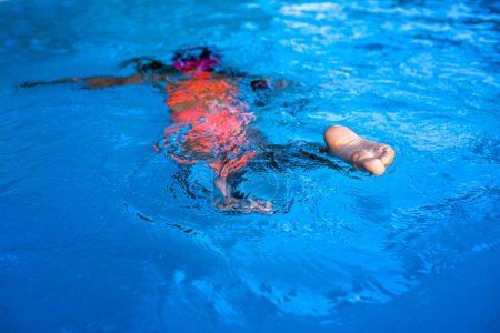 Foto de Un niño nada en una piscina azul claro, capturado desde un ángulo inusual centrándose en el pie. - Imagen libre de derechos