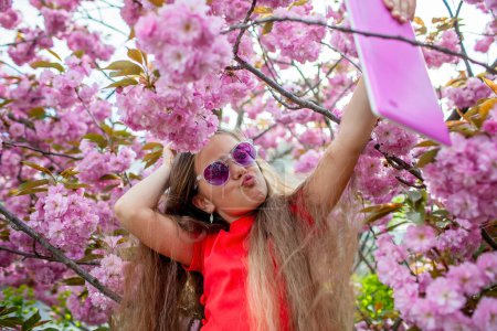 Foto de Una adolescente disfruta de la primavera tomando una selfie juguetona entre flores florecientes, su alegría capturada en un momento destinado a compartir en las redes sociales. - Imagen libre de derechos