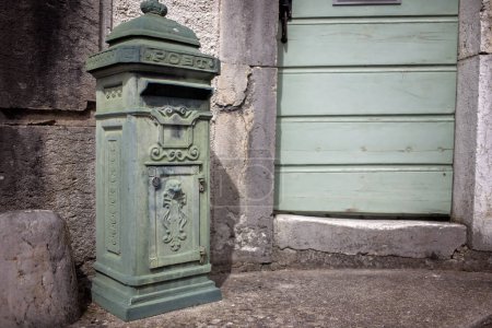 Foto de Un buzón verde pasado de moda junto a una puerta envejecida con persianas, que refleja el encanto del tradicional puesto de pueblo europeo. - Imagen libre de derechos