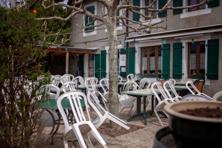 A quiet village cafe afternoon rush, its empty white chairs create a tranquil atmosphere. The green-shuttered windows, European charm, leisurely break