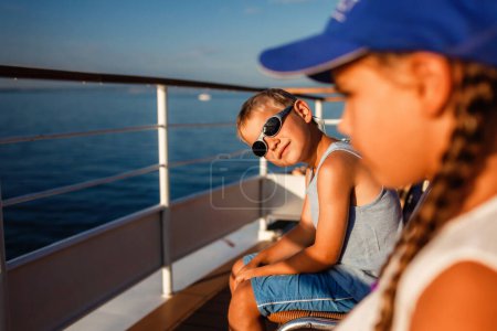 Foto de Un niño con gafas de sol y gorra azul se relaja en un barco con una chica, disfrutando de un día soleado en el agua, encarnando la alegría de las vacaciones de verano. - Imagen libre de derechos