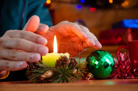 Close-up of freezing male hands warming up with flame of candle at cold Christmas Day during energy crisis
