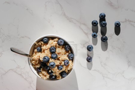 Photo for Top view of healthy vegan oatmeal with blueberries in white porcelain bowl. White marble table and copy space - Royalty Free Image