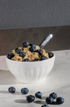 Photo for Healthy vegan oatmeal with blueberries in white porcelain bowl. White marble table and grey background - Royalty Free Image