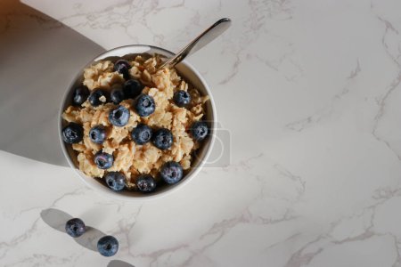 Photo for Top view of healthy vegan oatmeal with blueberries in white porcelain bowl. White marble table and copy space - Royalty Free Image
