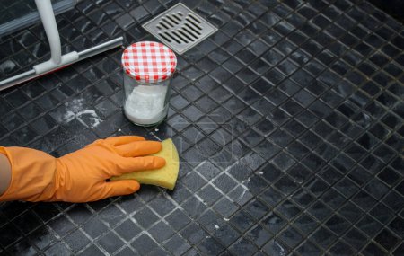 Foto de Primer plano de las manos de las mujeres en guantes naranja limpieza piso de la ducha con bicarbonato de sodio, concepto de limpieza ecológico - Imagen libre de derechos