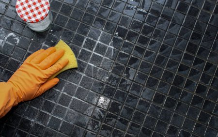 Foto de Primer plano de las manos de las mujeres en guantes naranja limpieza piso de la ducha con bicarbonato de sodio, concepto de limpieza ecológico - Imagen libre de derechos