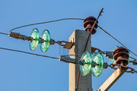 Glass insulators and wires of a high-voltage power line on a concrete pole against a background of blue sky