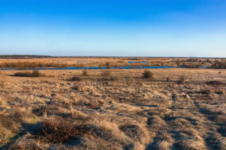 Vista de un valle del río con hierba seca en el prado y cielo azul claro en un día soleado, paisaje rural