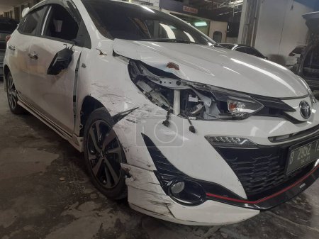 Photo for Jakarta, Indonesia, December 12, 2022 : A white Toyota Yaris entered the workshop after experiencing a serious accident on the road, the front right side of which was damaged. - Royalty Free Image