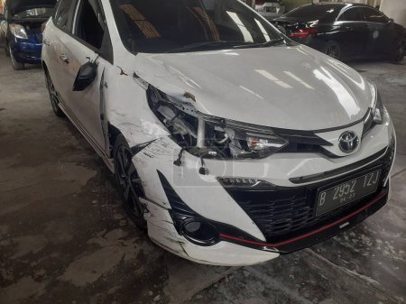 Photo for Jakarta, Indonesia, December 12, 2022 : A white Toyota Yaris entered the workshop after experiencing a serious accident on the road, the front right side of which was damaged. - Royalty Free Image