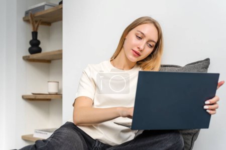 Téléchargez les photos : Jeune femme utilisant un ordinateur portable dans le salon confortable. - en image libre de droit