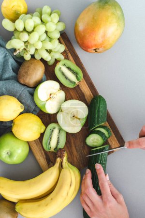 Photo for Unrecognizable female hands cut cucumber on a cutting board in the kitchen. Flat lay. - Royalty Free Image