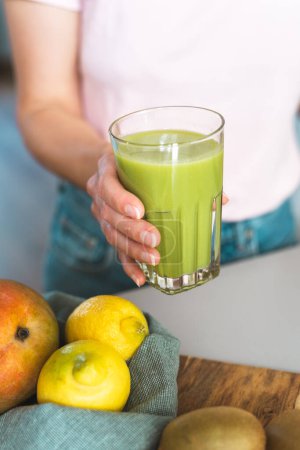 Téléchargez les photos : Main féminine méconnaissable tenant un verre de smoothie vert frais et sain. - en image libre de droit